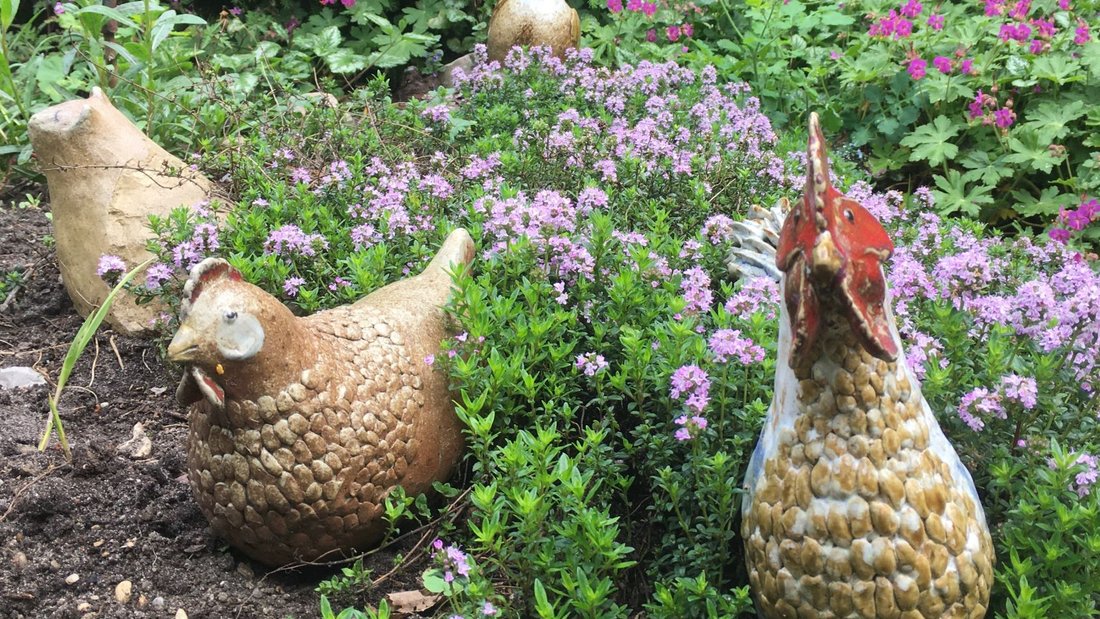 Getöpferte Hühner im Blumenbeet